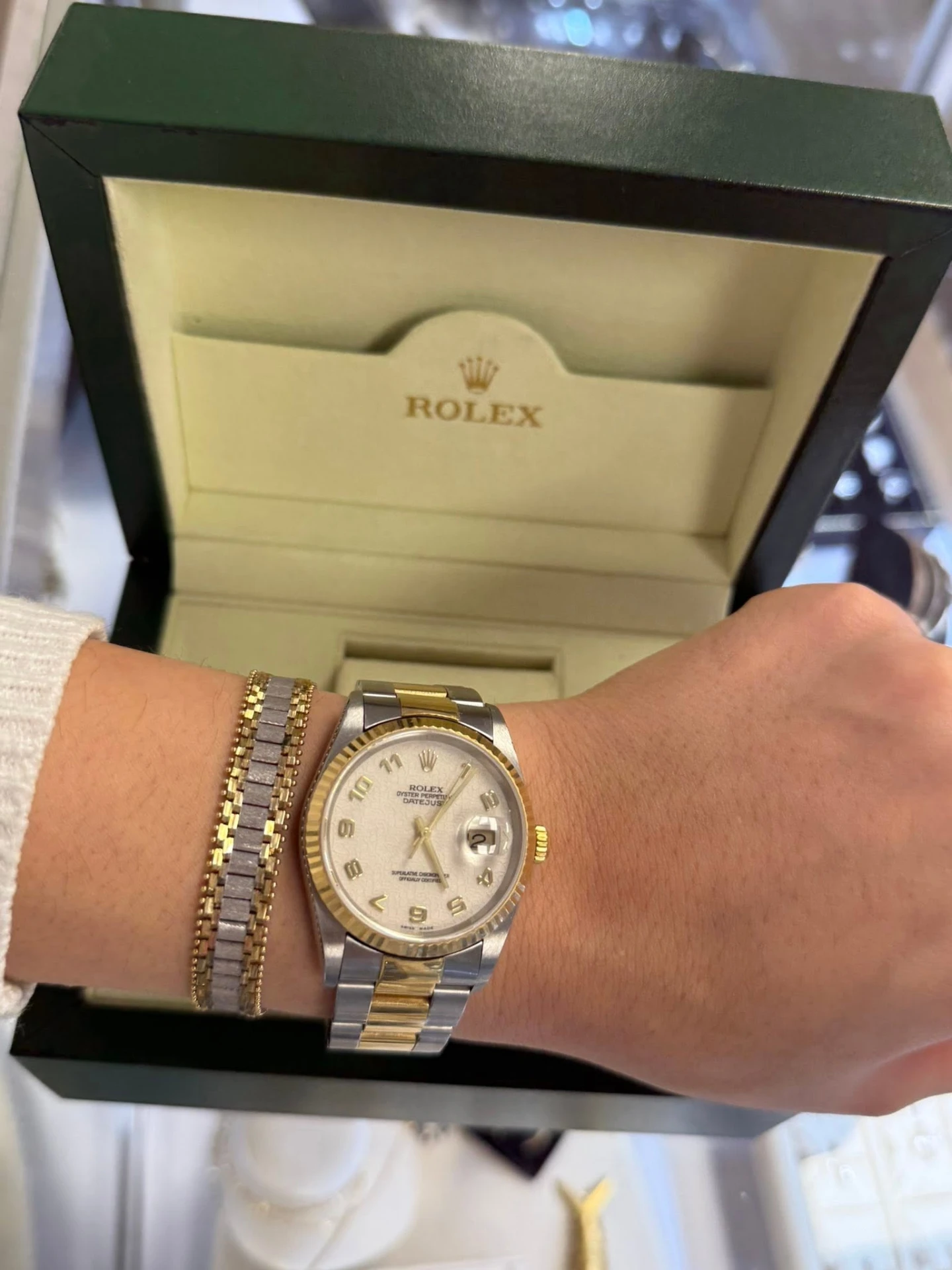 Two-tone Rolex Datejust worn on the wrist beside its green box
